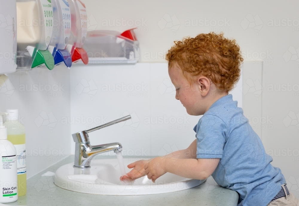 little boy washing his hands at hand basin with soap - Australian Stock Image