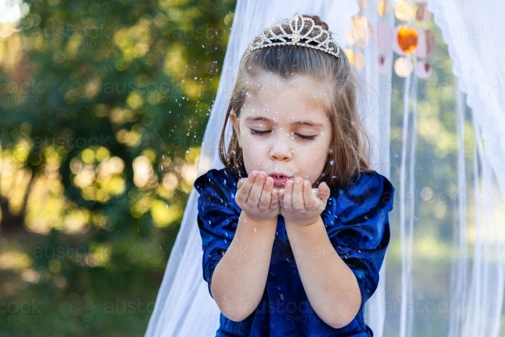 Little girl being a princess blowing sparkling glitter - Australian Stock Image