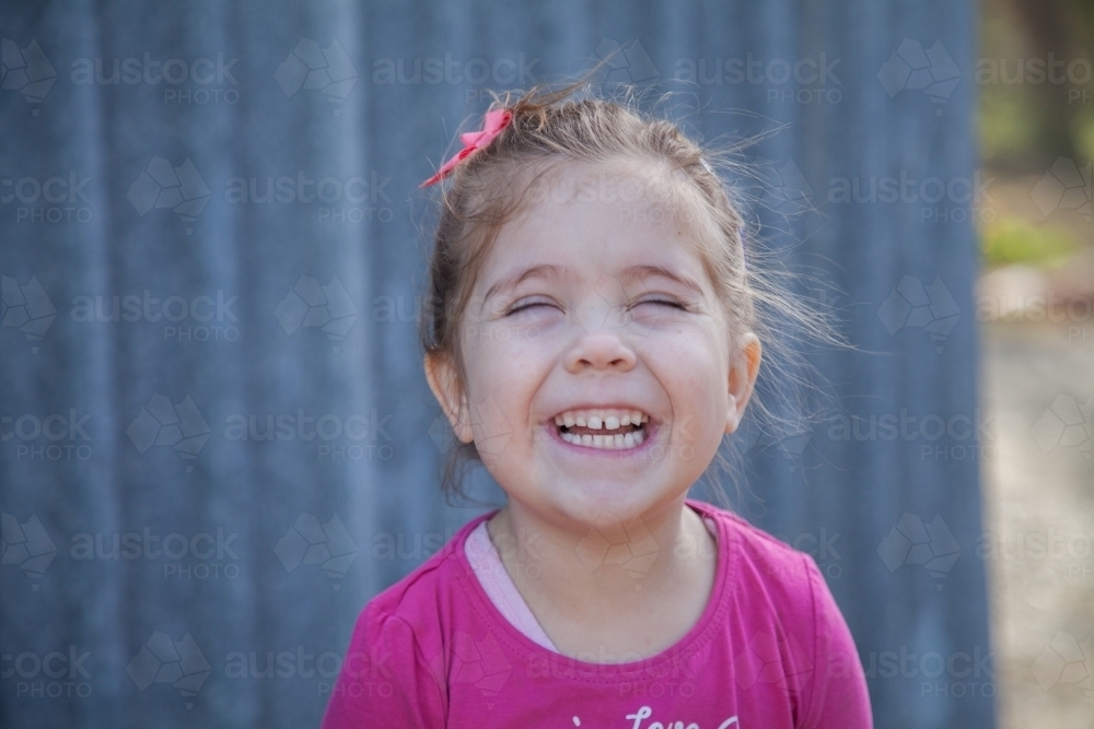 Little girl blinking shut her eyes and laughing - Australian Stock Image