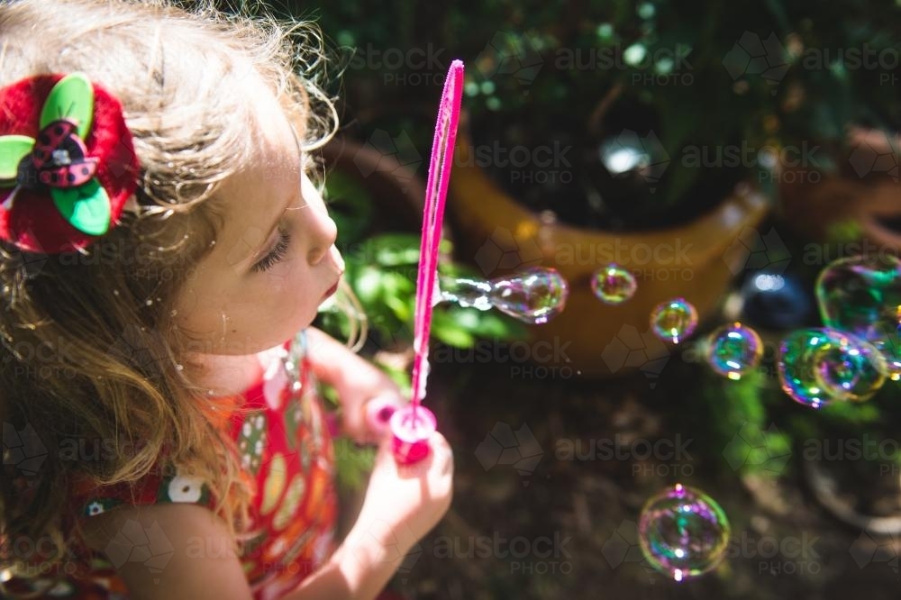 Little girl blowing bubbles in the garden - Australian Stock Image