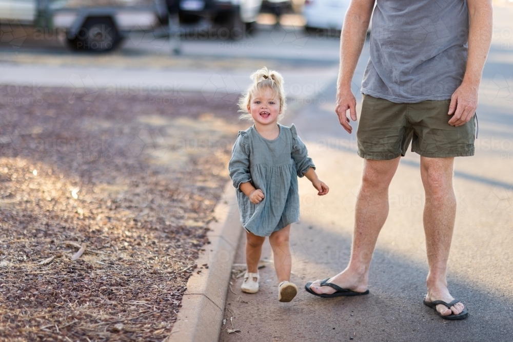little girl boldly stepping out with dad along edge of road - Australian Stock Image
