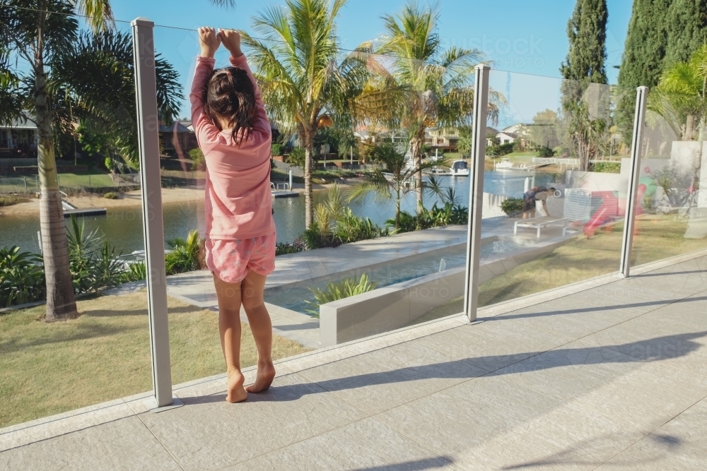 Little girl by pool glass fencing - Australian Stock Image