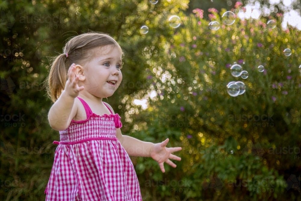Little girl chasing bubbles outside - Australian Stock Image