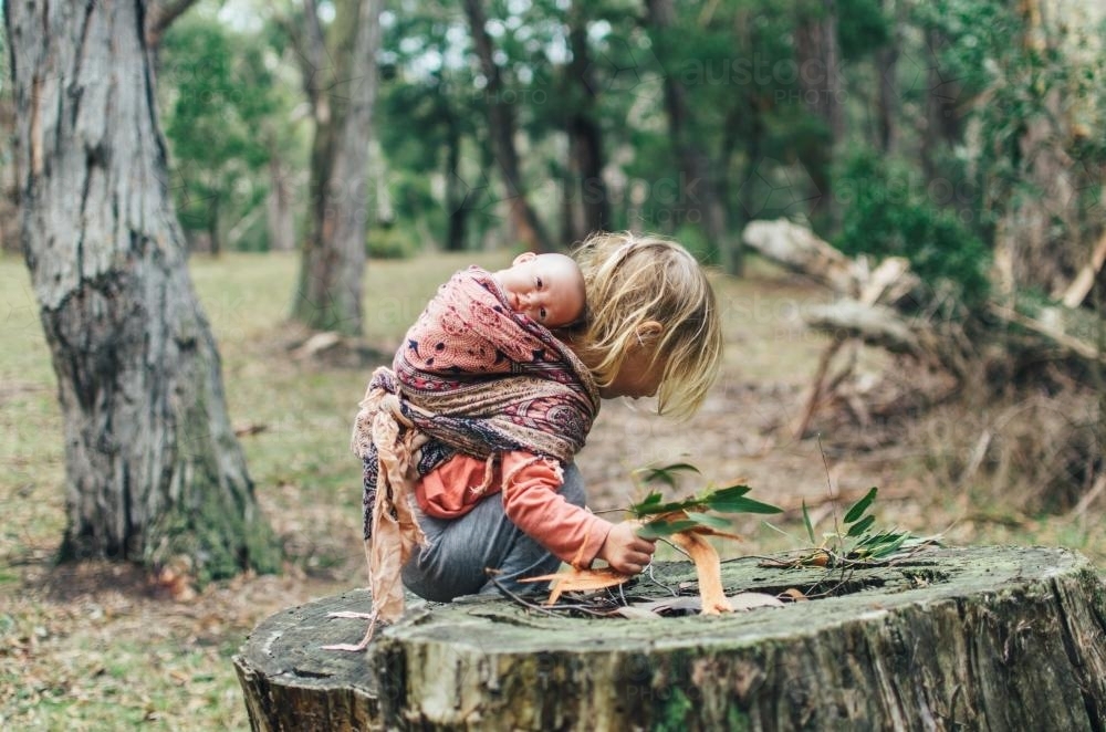 Little girl climbing tree stump with dolls in the bush - Australian Stock Image