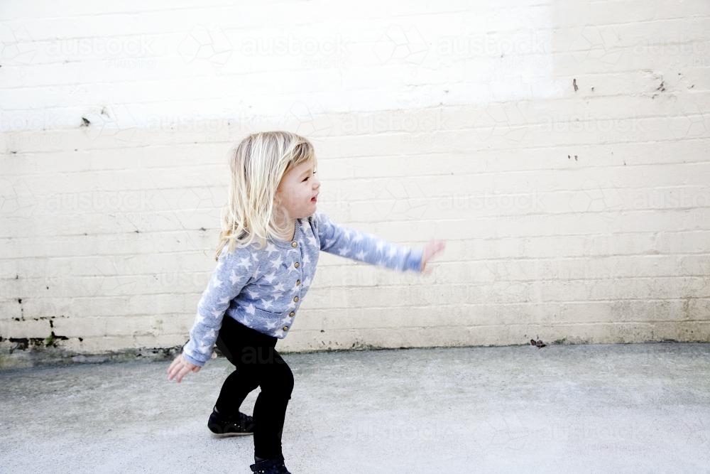 Little girl dancing in front of brick wall - Australian Stock Image