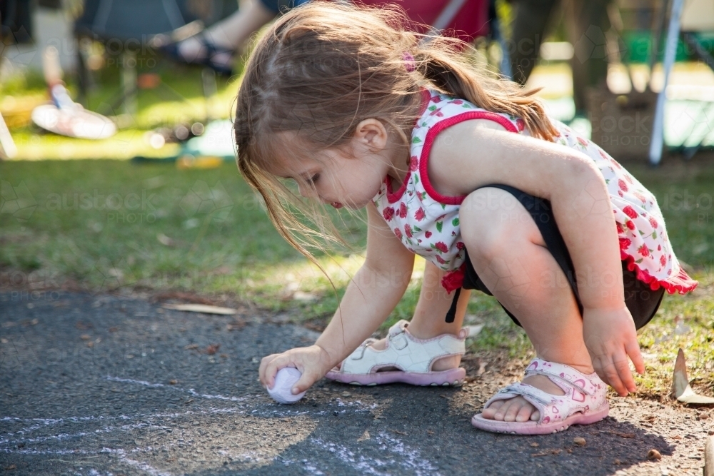 Little girl drawing on road beside campsite with chalk - Australian Stock Image