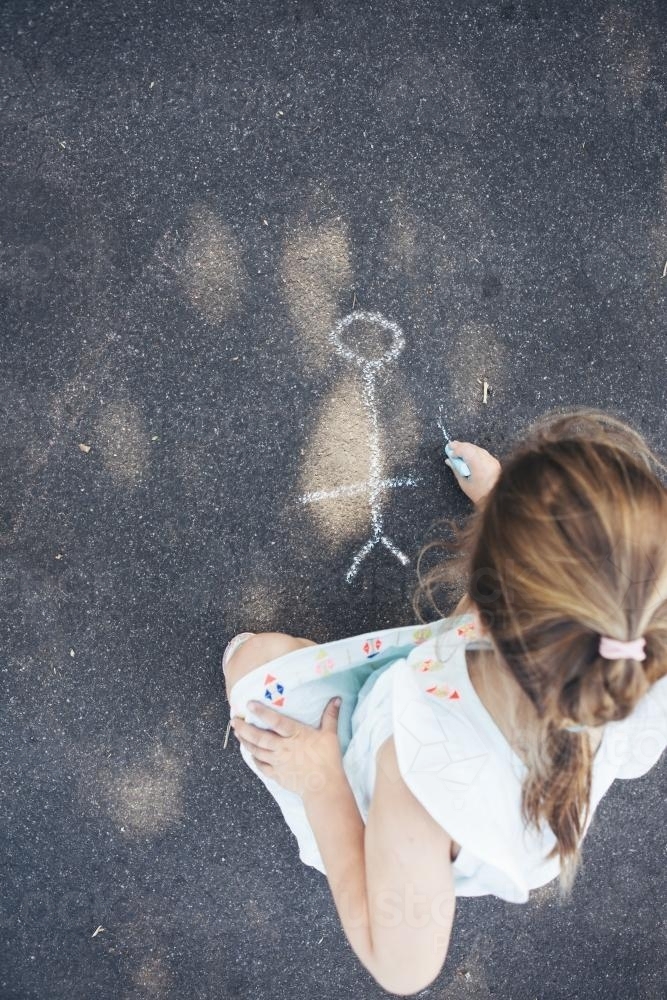 Little girl drawing pictures on the asphalt with chalk - Australian Stock Image