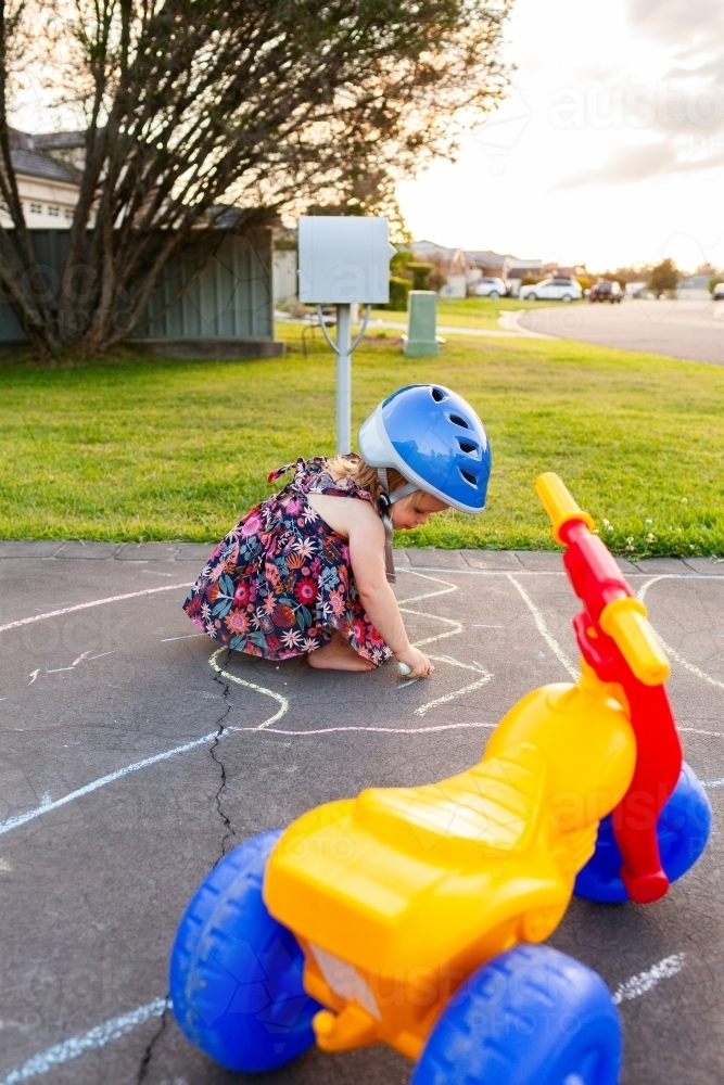 Little girl drawing with chalk on suburban driveway at sunset - Australian Stock Image