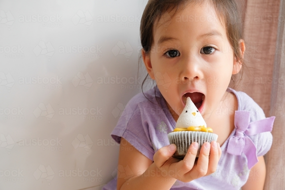 Little girl eating Easter chick lemon chocolate cupcake - Australian Stock Image