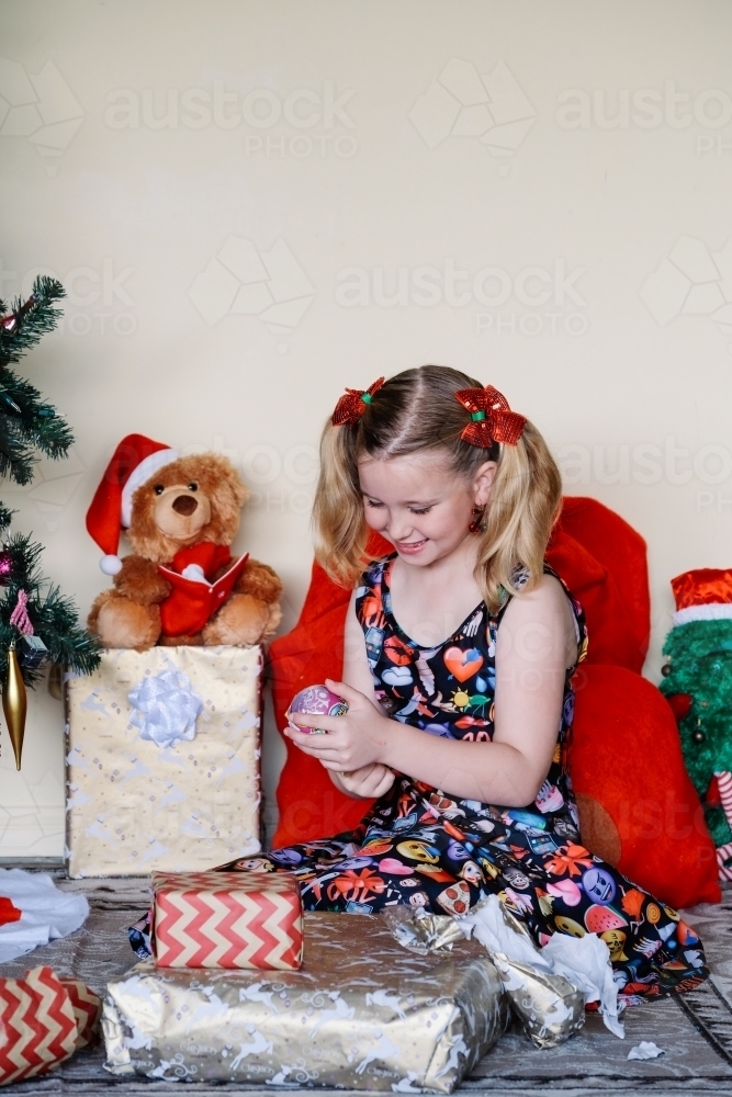 Little girl happily looking at a Christmas gift she has unwrapped - Australian Stock Image