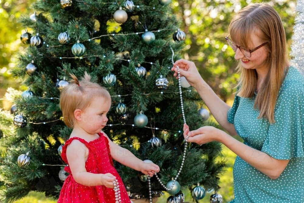 Little girl helping decorate Christmas tree with string beads - Australian Stock Image