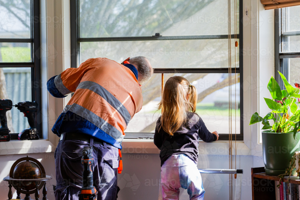 Little girl helping grandfather fix the window at home - Australian Stock Image