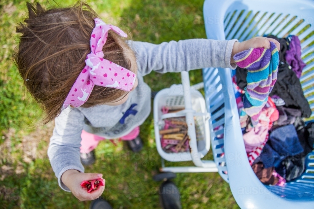 Little girl helping with washing by handing pegs and socks up - Australian Stock Image