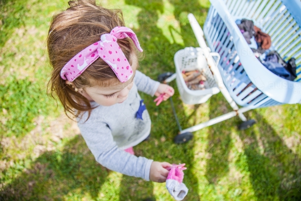Little girl helping with washing by handing pegs and socks up - Australian Stock Image