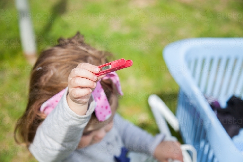 Little girl helping with washing by handing pegs up - Australian Stock Image
