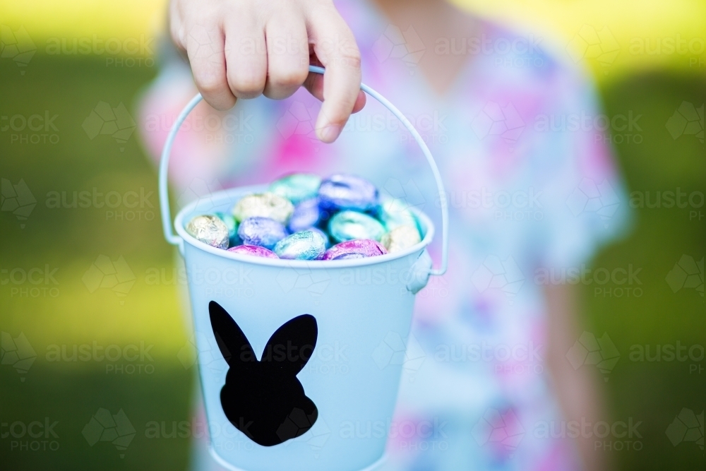 Little girl holding a bucket of foil wrapped Easter eggs - Australian Stock Image