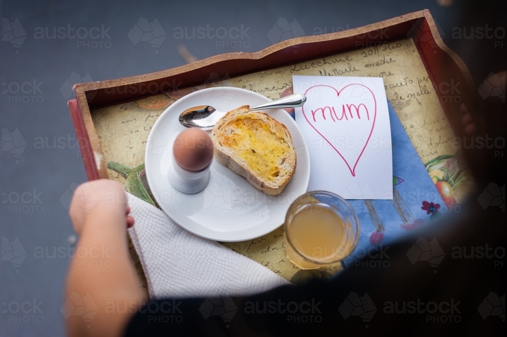 little girl holding a tray with egg and toast breakfast on mother's day - Australian Stock Image