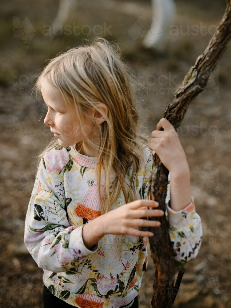 Little girl holding a tree branch in the forest. - Australian Stock Image