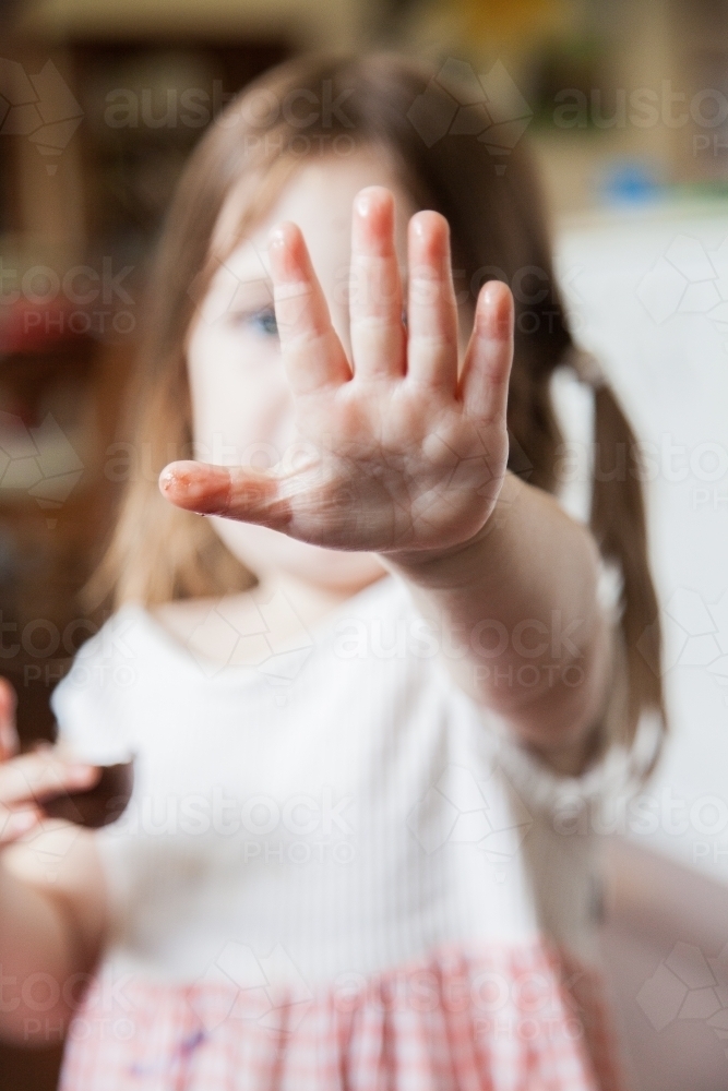 Little girl holding out sticky chocolate fingers to camera - Australian Stock Image
