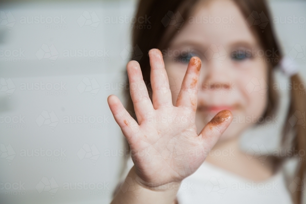 Little girl holding out sticky chocolate fingers to camera - Australian Stock Image