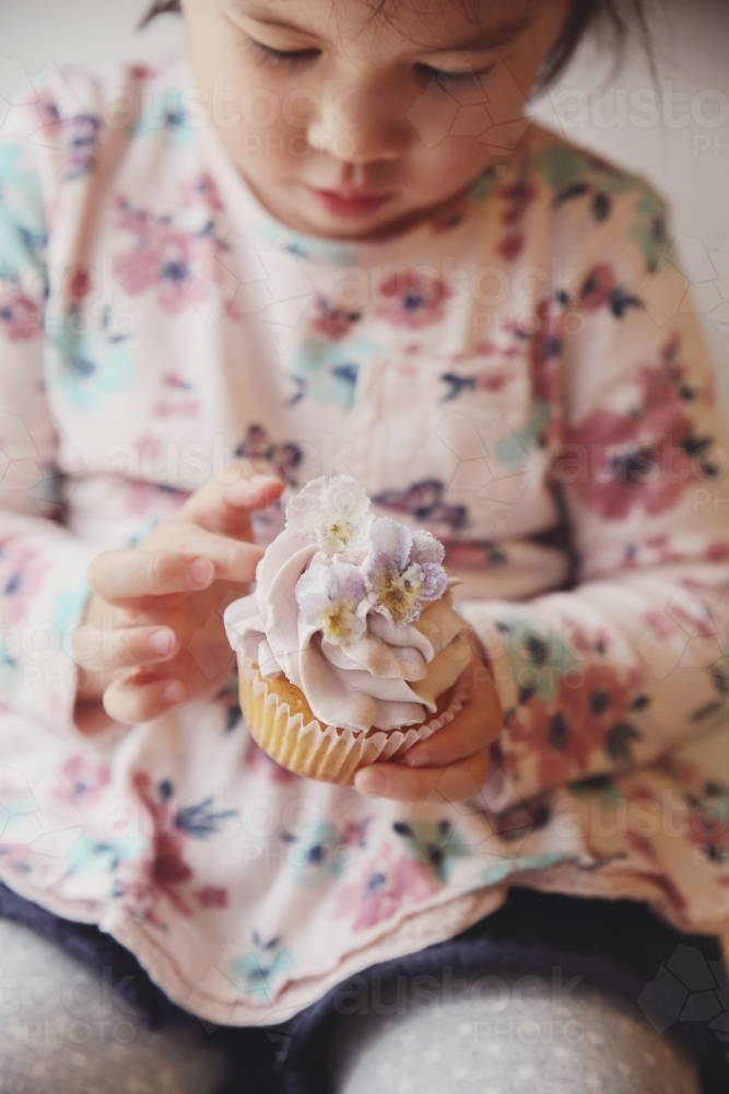 Little girl holding purple flower cupcake - Australian Stock Image