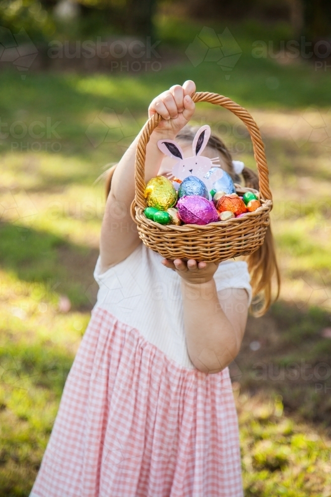 Little girl holding up basket full of colourful Easter eggs - Australian Stock Image