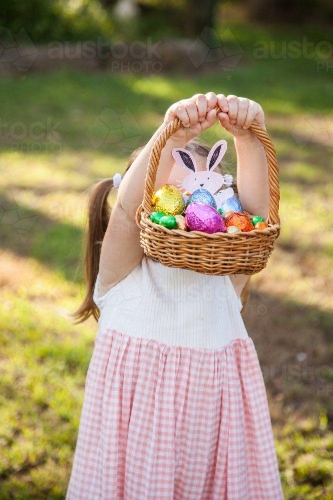 Little girl holding up basket full of colourful Easter eggs - Australian Stock Image