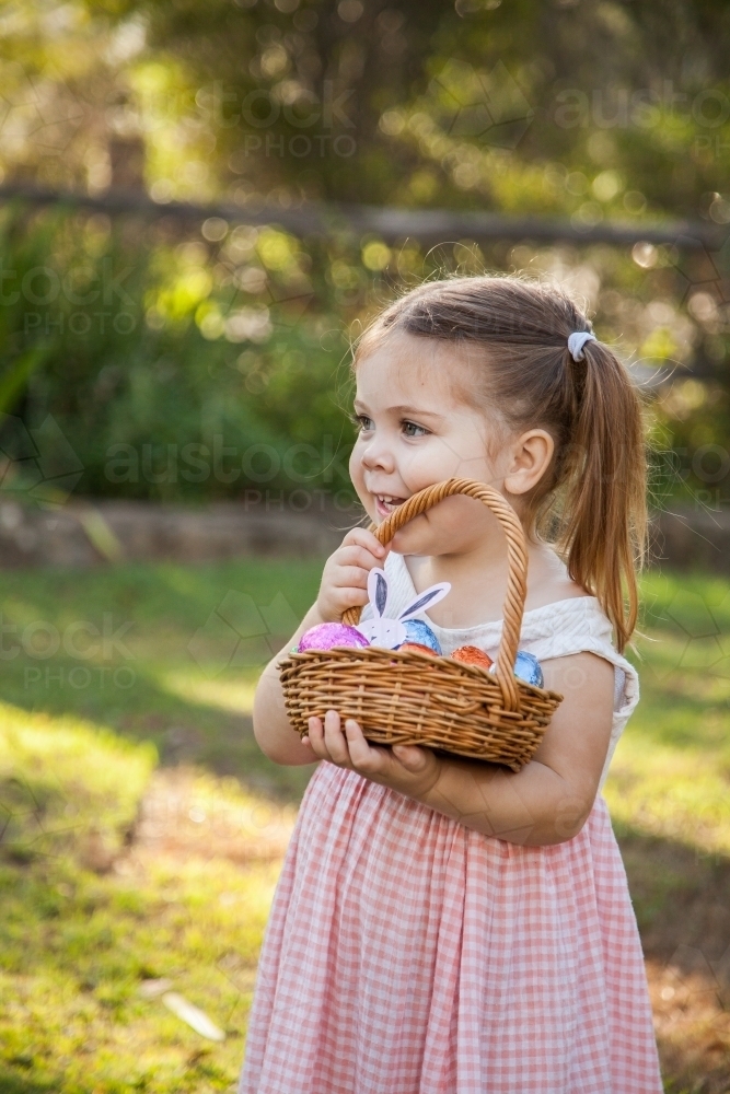 Little girl holding up basket full of colourful Easter eggs - Australian Stock Image