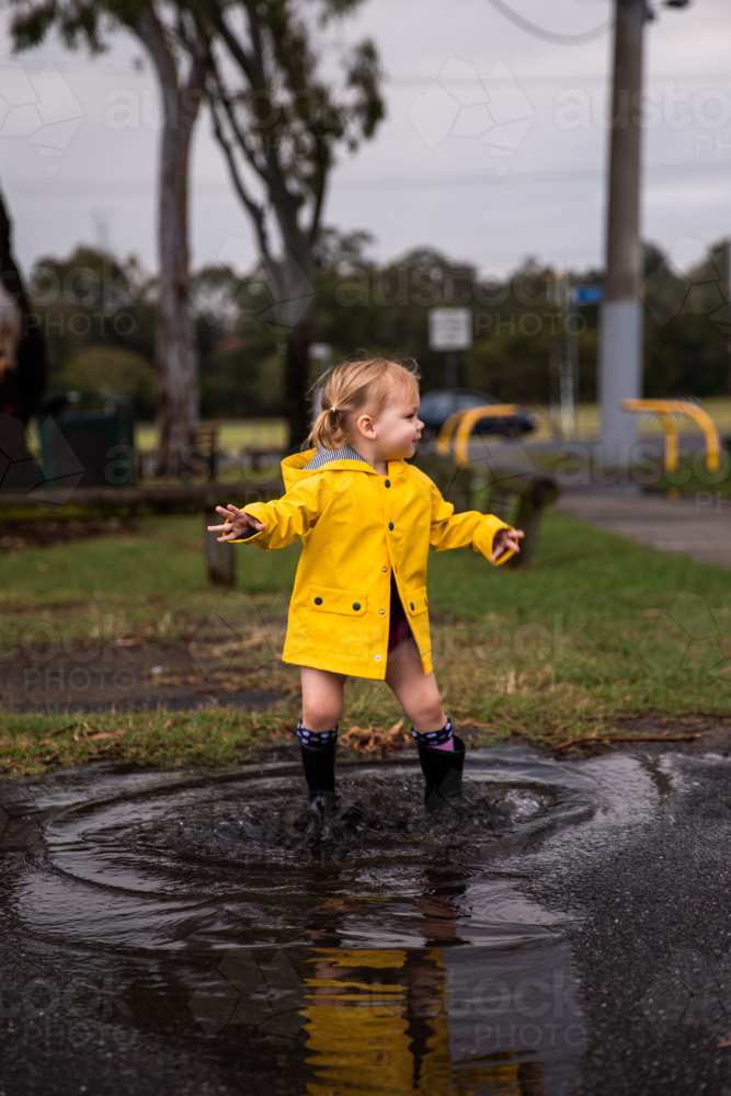 little girl in a raincoat jumping in puddles - Australian Stock Image