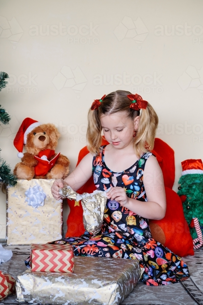 Little girl in an emoji dress opening a Christmas present - Australian Stock Image