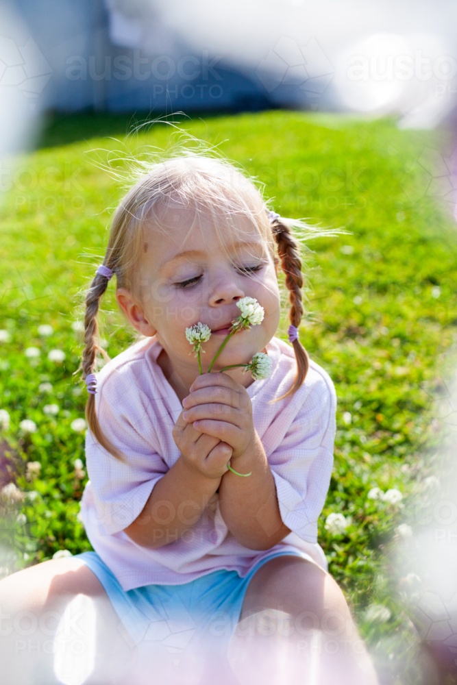 Image of Little girl in backyard picking clover flowers in sunlight ...