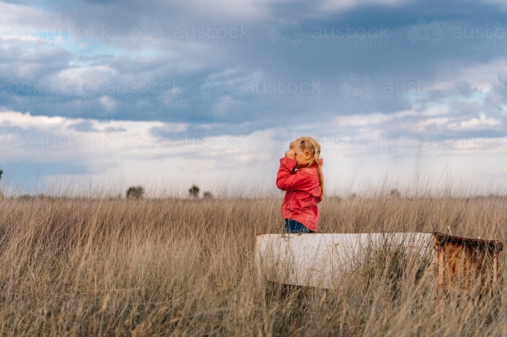 Little girl in long grass, peering out over farm property - Australian Stock Image
