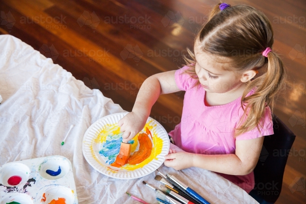 Little girl in pink painting on a paper plate - Australian Stock Image