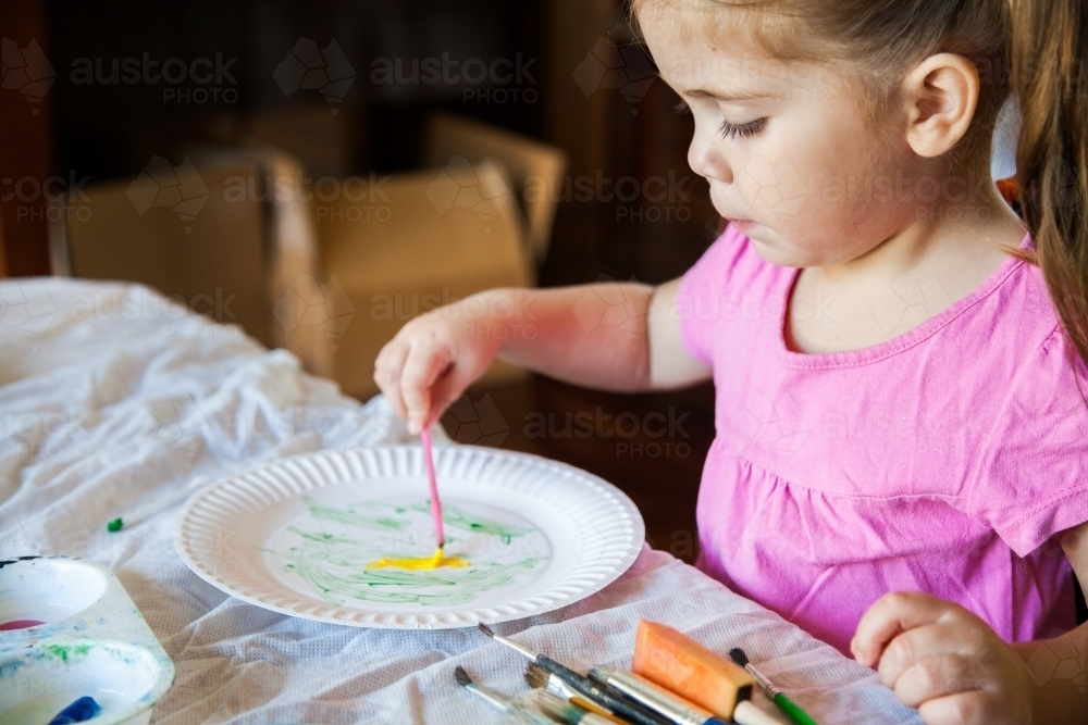 Little girl in pink painting on a paper plate - Australian Stock Image