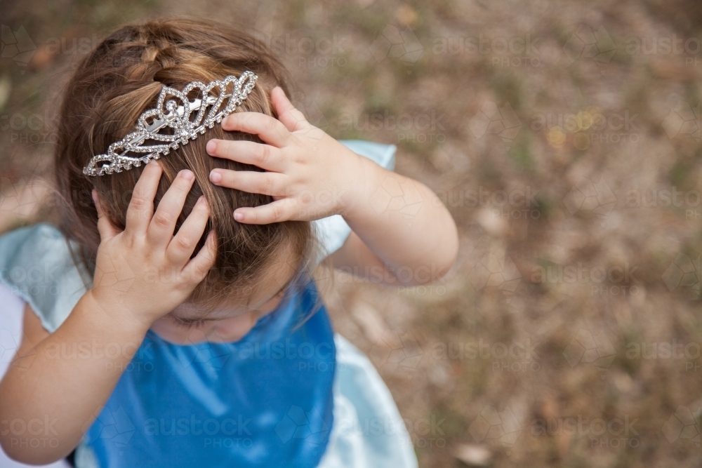 Little girl in princess dress ups costume and tiara looking down - Australian Stock Image