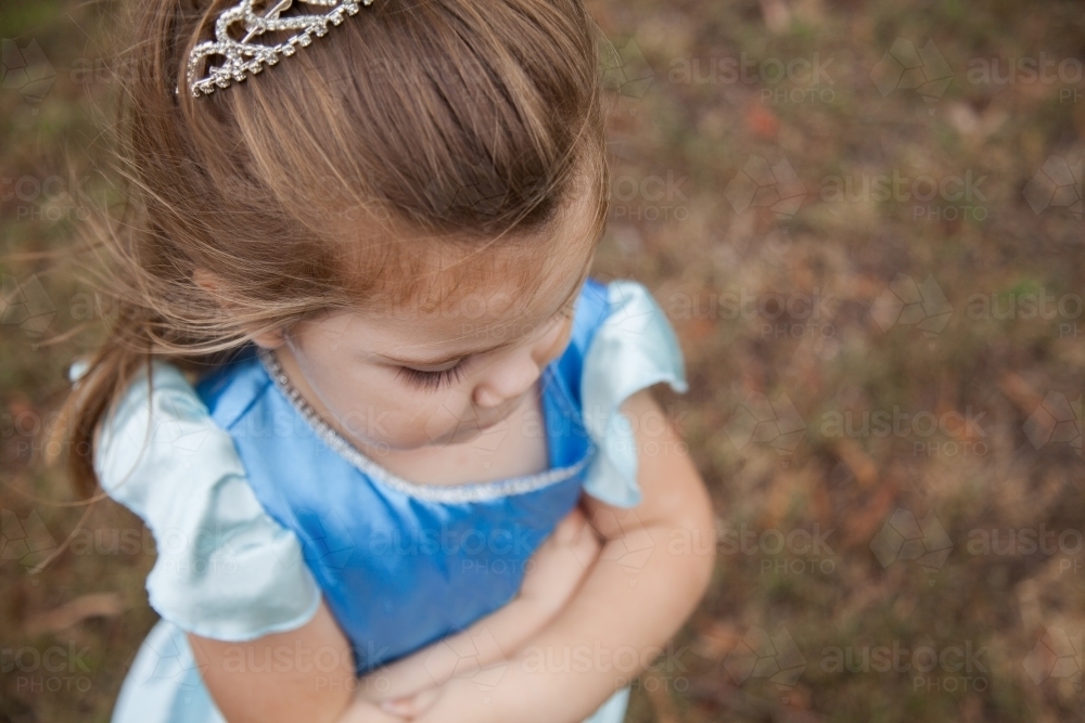 Little girl in princess dress ups costume and tiara looking down - Australian Stock Image