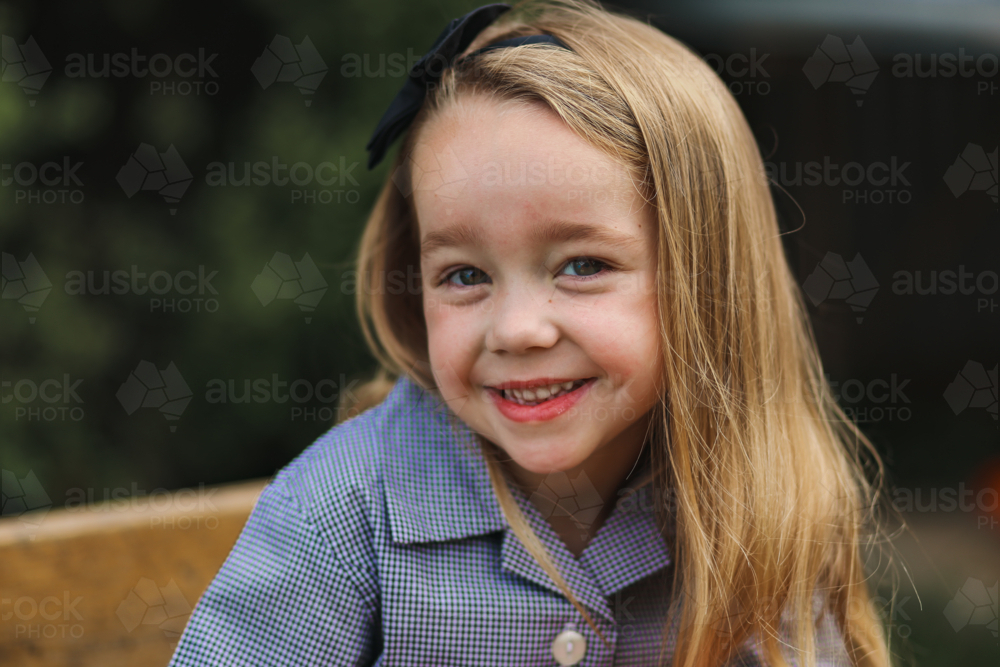 Image of Little girl in school uniform sitting at desk outdoors smiling ...