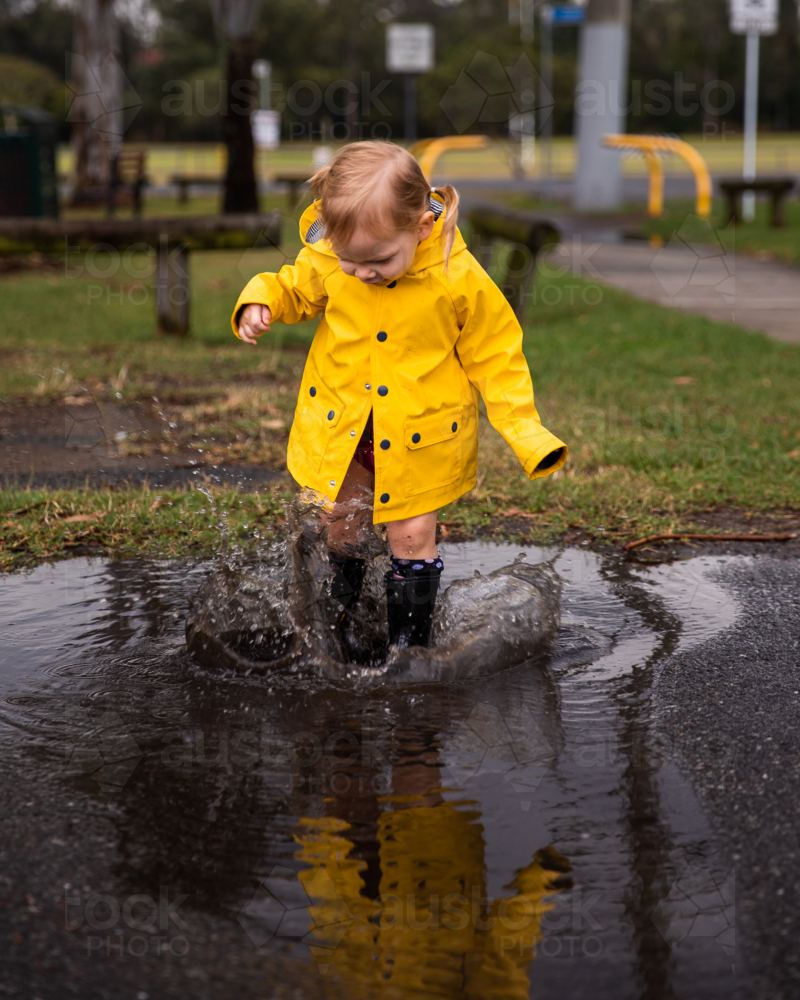 little girl jumping into a puddle causing a big splash - Australian Stock Image