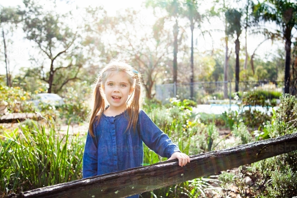 Little girl leaning on garden fence outside smiling - Australian Stock Image