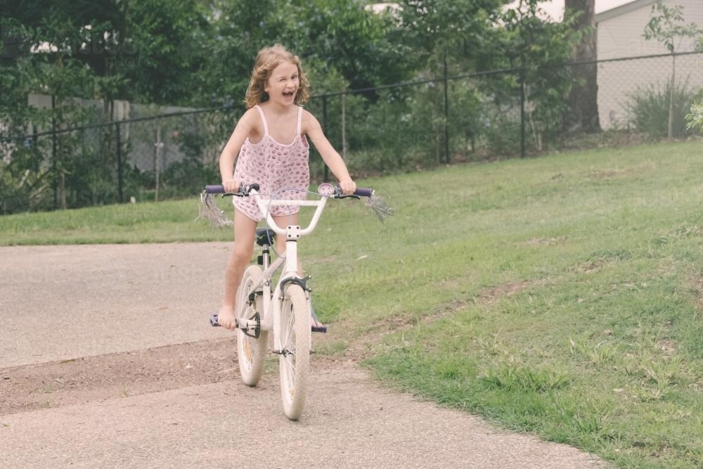 Little girl learning to ride her new bike, winking at camera - Australian Stock Image
