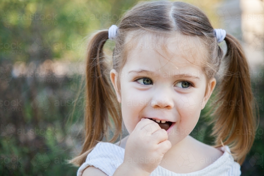 Little girl looking sideways as she eats a chocolate Easter egg - Australian Stock Image