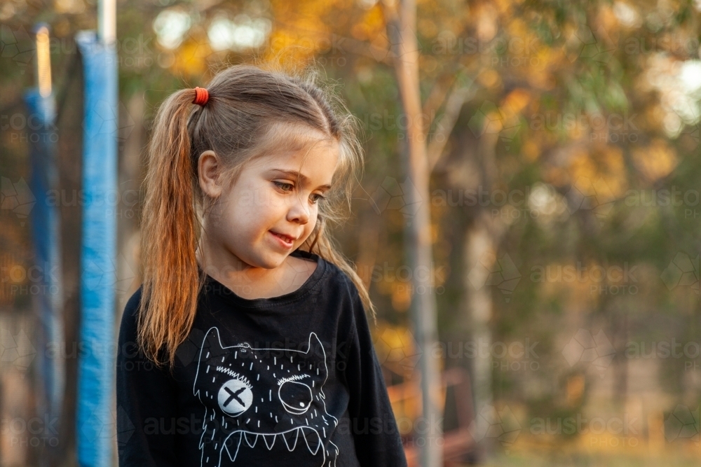 Little girl looking to the side and down playing outside - Australian Stock Image