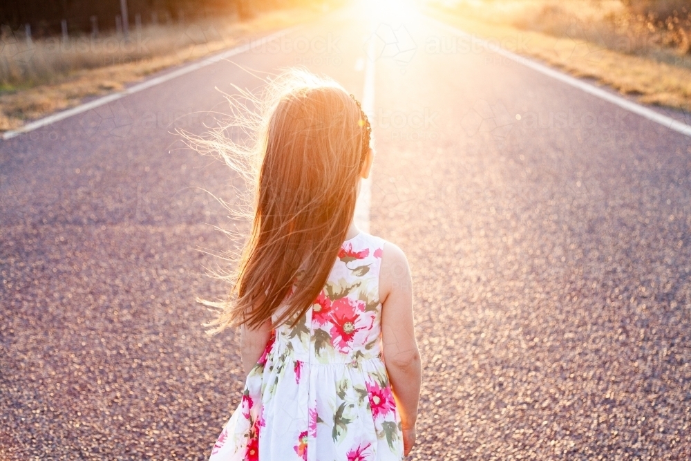 Little girl looking towards sunset along road - Australian Stock Image