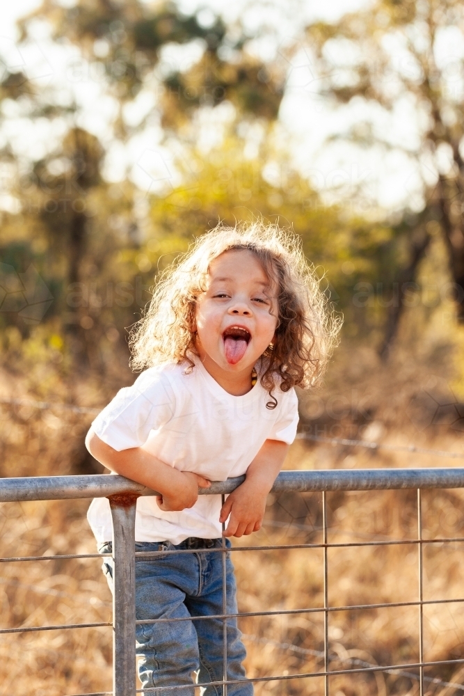 Little girl on farm gate poking tongue out - Australian Stock Image