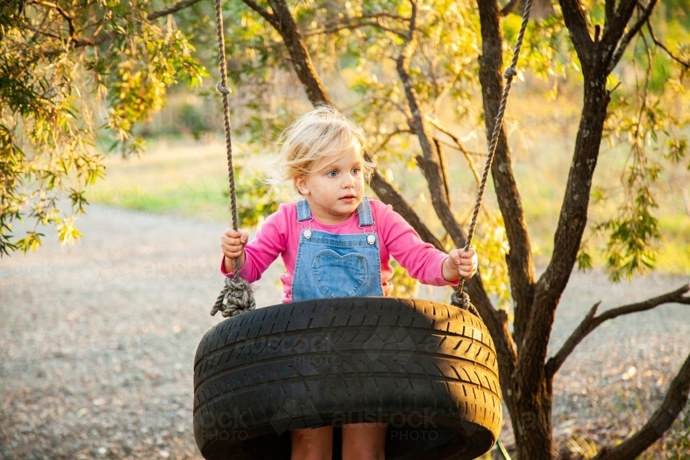 Little girl on tyre swing in afternoon light - Australian Stock Image