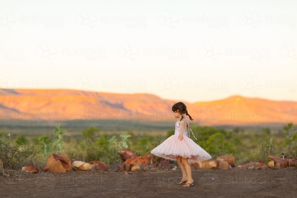 little girl outdoors swirling her pink skirt in soft evening light - Australian Stock Image