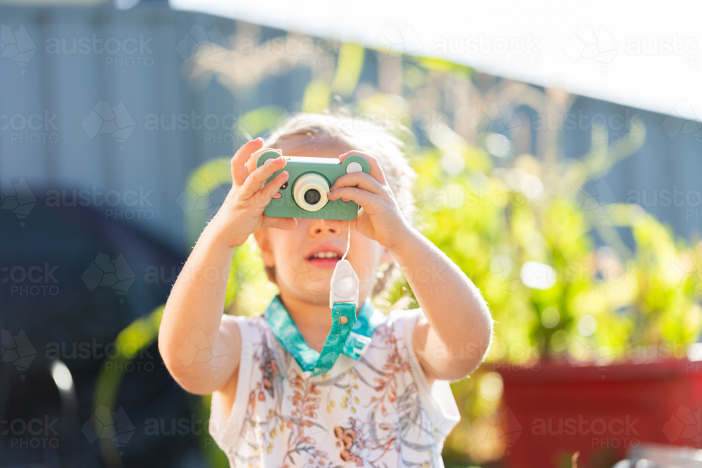 Little girl outside holding up tiny digital camera taking a photo - Australian Stock Image