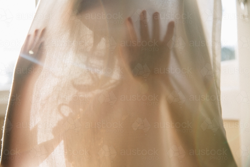 Little girl playing hide and seek behind curtains at home - Australian Stock Image