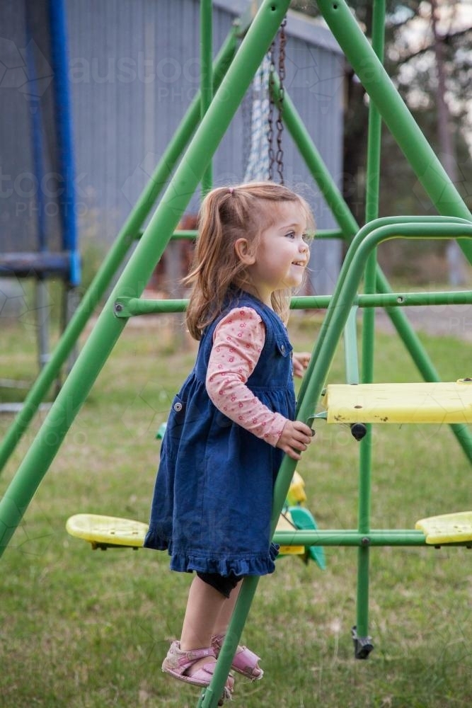 Little girl playing on a swing set and slide in the backyard - Australian Stock Image