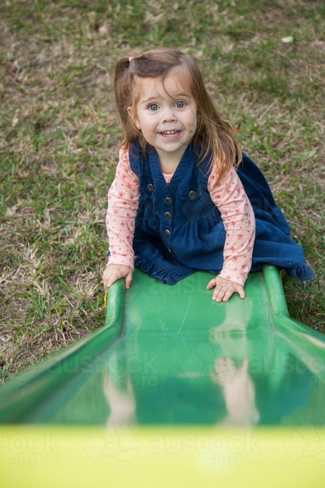 Little girl playing on a swing set and slide in the backyard - Australian Stock Image